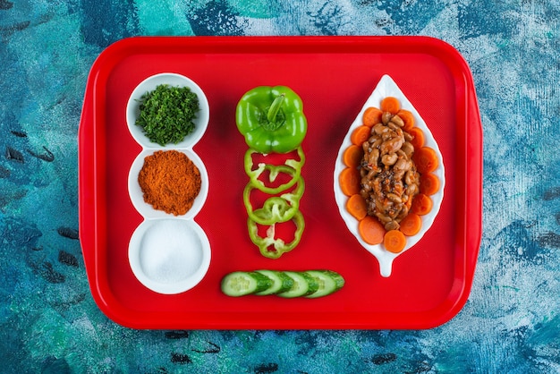 Free photo sliced carrots and beans and vegetables on a plate on a tray, on the blue table.