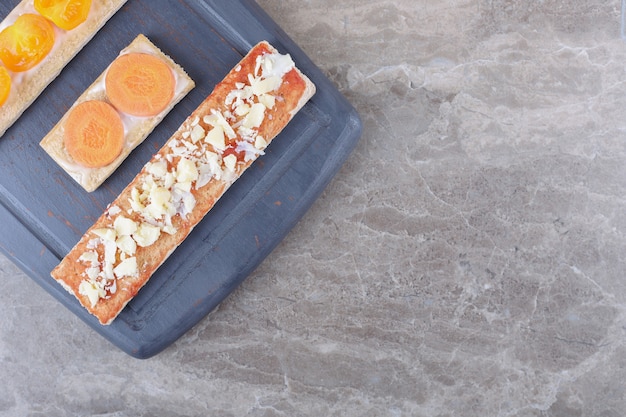 Sliced carrots, cheese and tomatoes on crispy breads on the wooden tray, on the marble surface