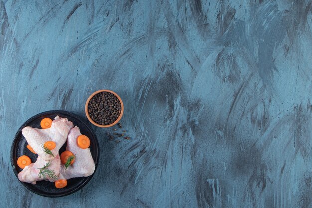 Sliced carrots and chicken wing on a plate next to spice bowl , on the blue background. 