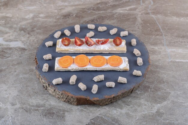 Carote affettate e pomodori su fette biscottate, circondati dalla mollica sul bordo, sulla superficie di marmo