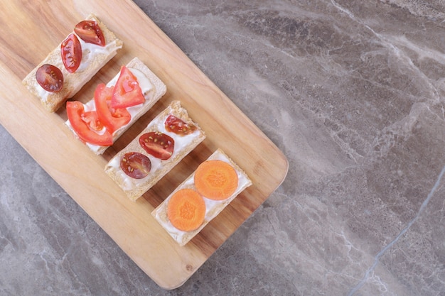 Sliced carrots and tomatoes on crispy breads , on the marble surface