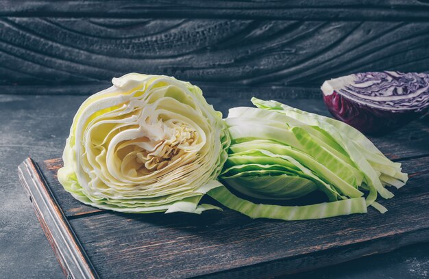 Sliced and chopped cabbage in a cutting board with red cabbage side view on a dark textured background