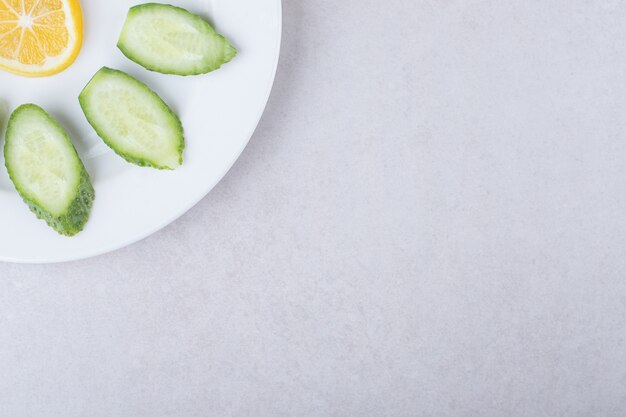 Sliced cucumber, lemon and parsley on a plate on marble table.