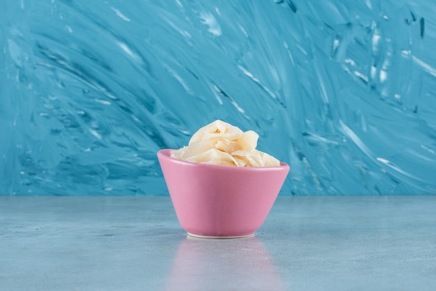 Sliced fermented sauerkraut with carrots in a plastic bowl on the blue surface