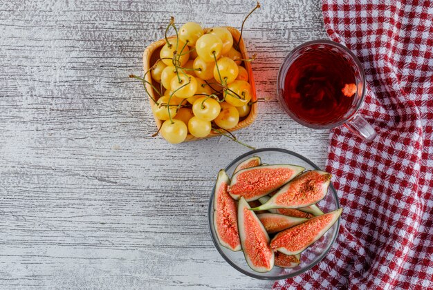 Sliced figs in a bowl with cherries, cup of tea top view on grungy and kitchen towel