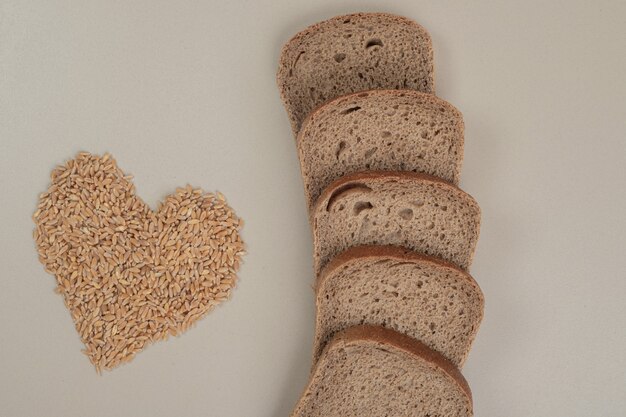 Sliced fresh brown bread with oat grains on white surface