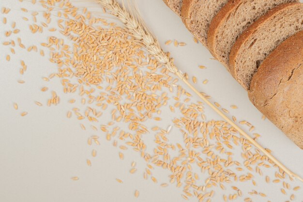 Sliced fresh brown bread with oat grains on white surface