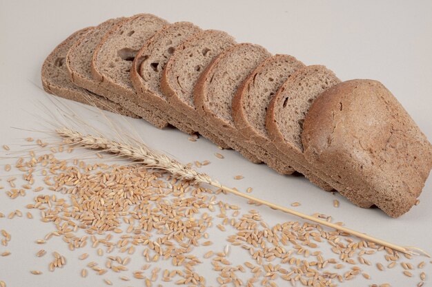 Sliced fresh brown bread with oat grains on white surface