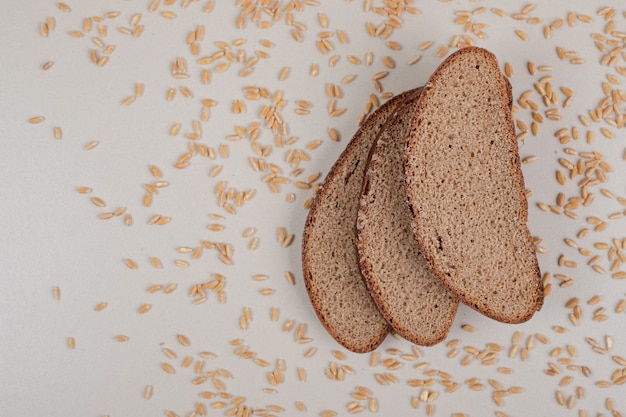 Sliced fresh brown bread with oat grains on white surface