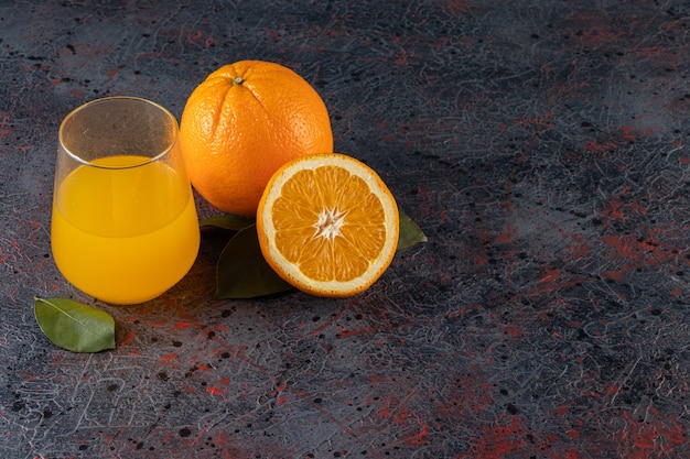 石のテーブルの上に置かれた葉とジュースのガラスピッチャーでスライスされた新鮮なオレンジ色の果物。