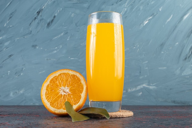 Sliced fresh orange fruit with leaves and a glass pitcher of juice placed on stone table.