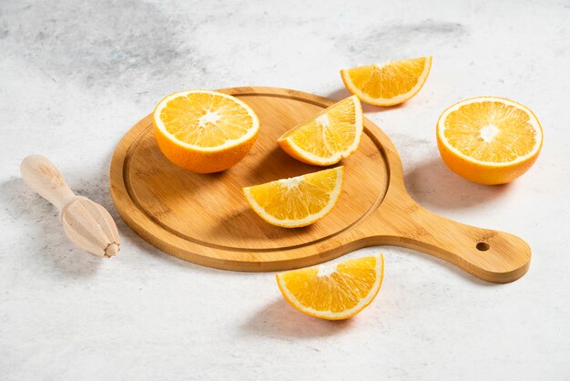 Sliced fresh oranges with wooden reamer on marble.