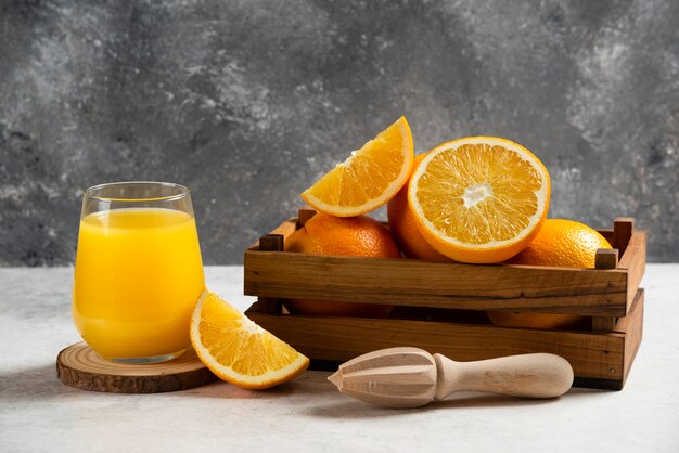 Sliced fresh oranges with wooden reamer on marble.