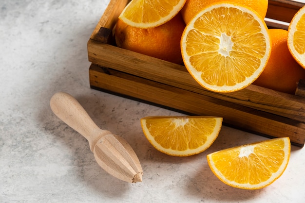 Sliced fresh oranges with wooden reamer on marble.