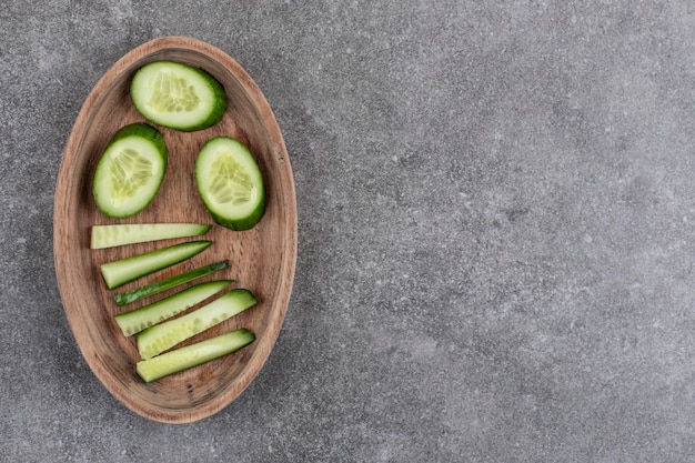 Sliced fresh organic cucumber in wooden bowl over grey surface. 