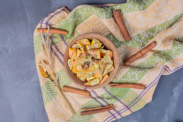 Sliced fruit bowl with cinnamon and cloth on blue.