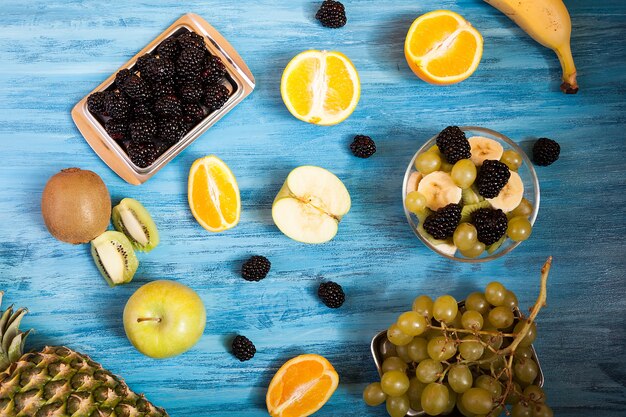青い木製の背景にスライスされた果物とベリーの上面図。新鮮なトロピカルフルーツの木製テーブル。果物の健康的な自然の新鮮さのミックス