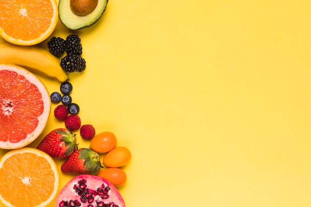 Sliced fruits and berries on yellow background 