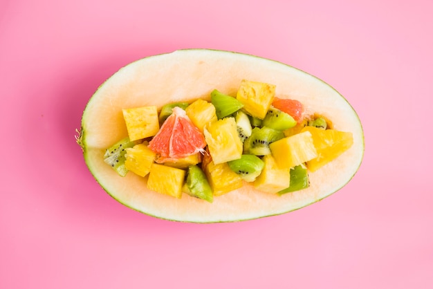 Sliced fruits with halved melon on pink background