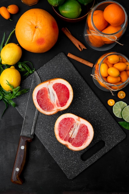 Sliced grapefruits and orange with other citrus fruits on black surface top view