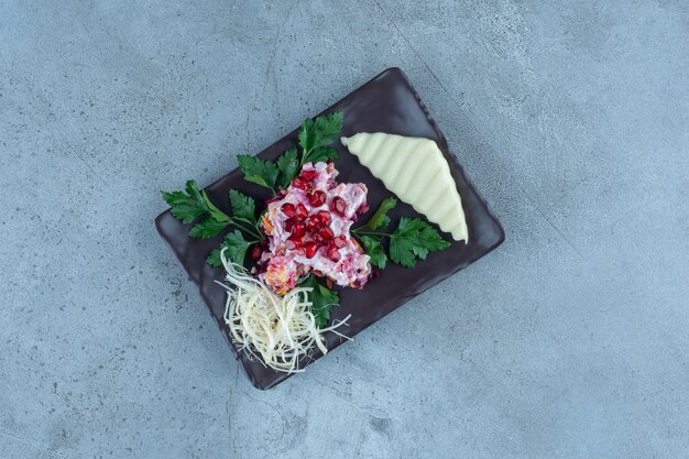 Sliced and grated cheese on a black platter with a small portion of salad, on marble.