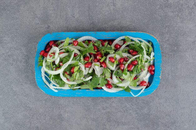 파란색 접시에 얇게 썬 채소, 양파, 석류 씨앗. 고품질 사진