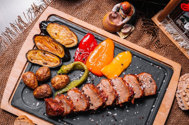 Sliced grilled steak on the wooden board bell pepper potato eggplant salt top view