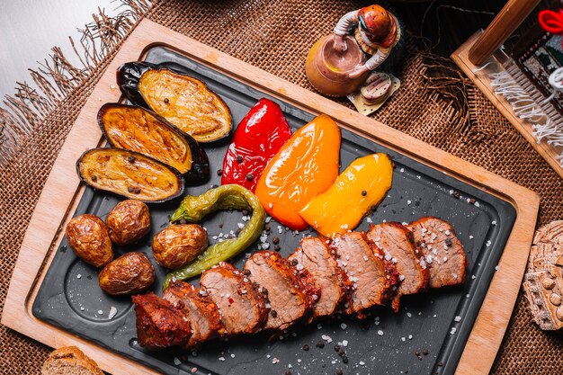 Sliced grilled steak on the wooden board bell pepper potato eggplant salt top view