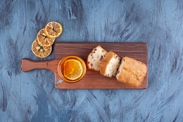 Sliced homemade cake with raisins and a glass cup of tea placed on a wooden cutting board . 