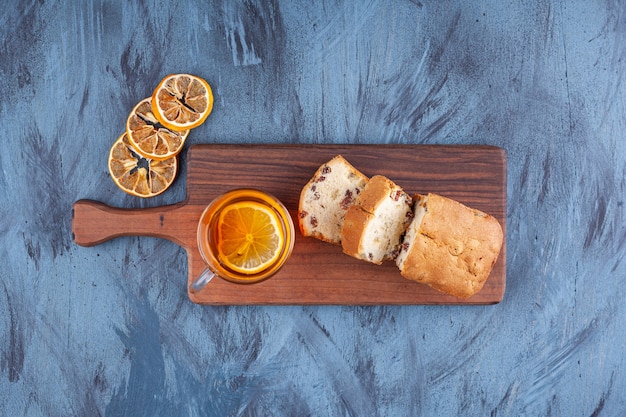 Sliced homemade cake with raisins and a glass cup of tea placed on a wooden cutting board . 