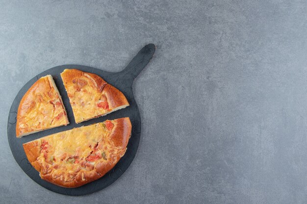 Sliced homemade pizza on black cutting board. 