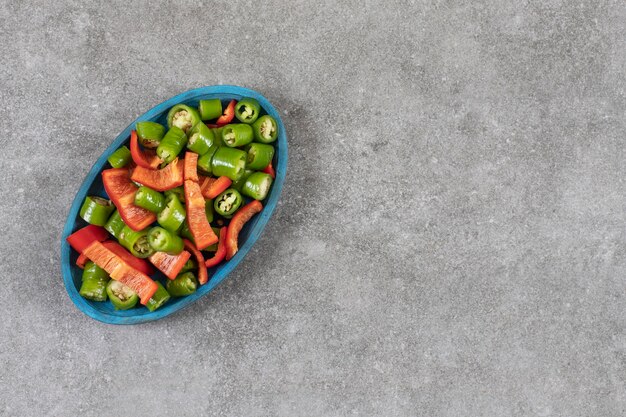 Sliced hot pepper and bell pepper on a plate, on the marble table. 