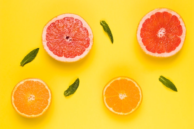 Sliced juicy grapefruit orange and green leaves on yellow surface 