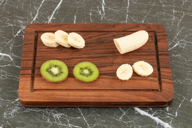 Sliced kiwi and banana on wooden board.