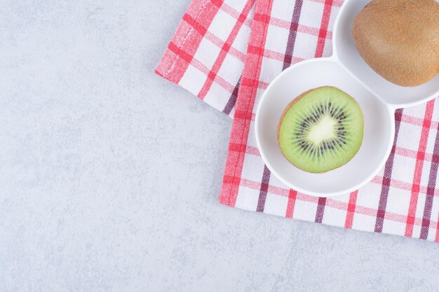 A sliced kiwi in white plate on tablecloth.