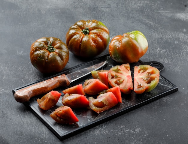 Sliced kumato tomatoes with knife on grey and cutting board wall.