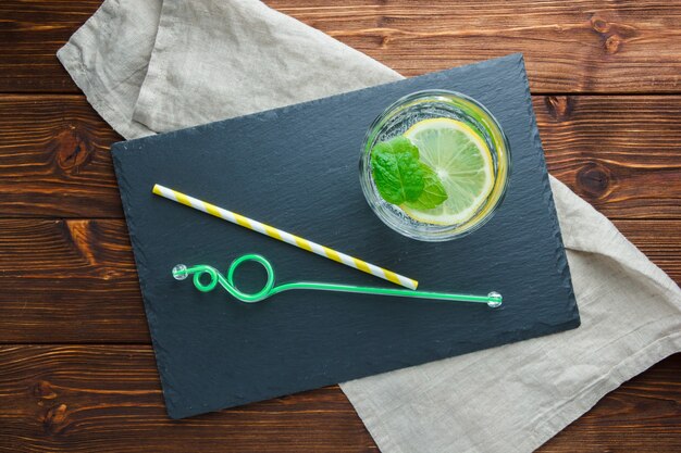 Sliced lemon in a bowl with black cardboard, straws top view on a wooden surface