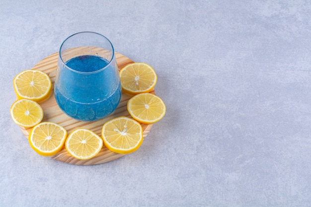 Sliced lemon next to a glass of blue smoothie on a wooden plate , on the marble background.