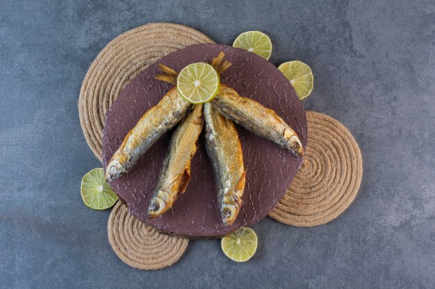 Sliced lemons and dried salted fish on a board on a trivet, on the marble surface