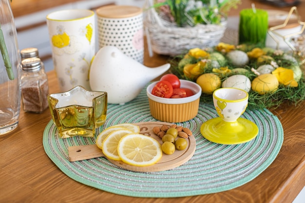 Нарезанные лимоны, оливки, миндаль на деревянной доске, пасхальные яйца на большом семейном столе