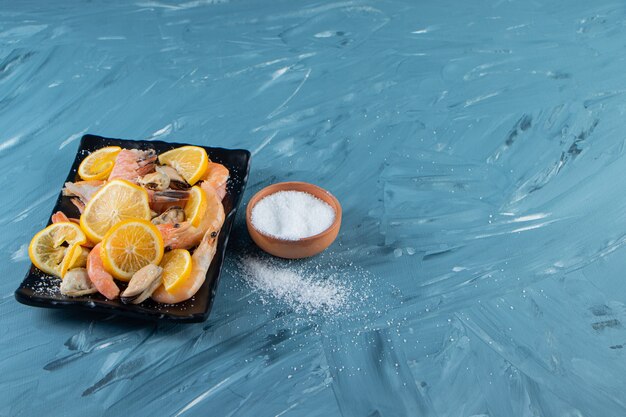 Sliced lemons and shrimps on a platter next to salt bowl , on the marble background. 