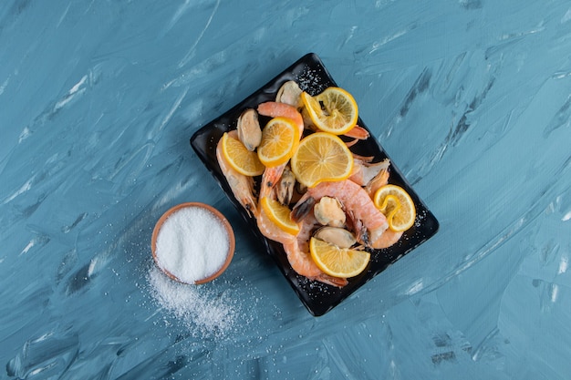 Limoni e gamberetti affettati su un piatto da portata accanto alla ciotola del sale, sulla superficie di marmo.