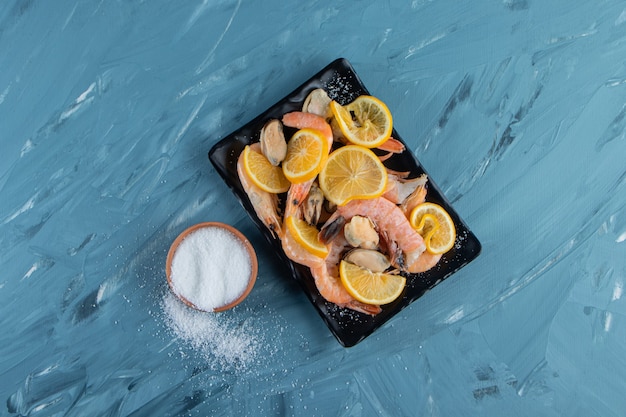 Sliced lemons and shrimps on a platter next to salt bowl , on the marble surface.