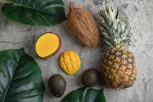 Sliced mango, coconut, pineapple and ripe avocados on marble surface.