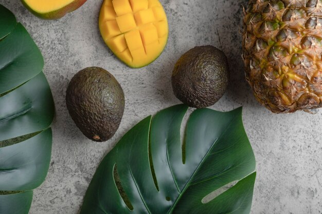 Sliced mango, coconut, pineapple and ripe avocados on marble surface.