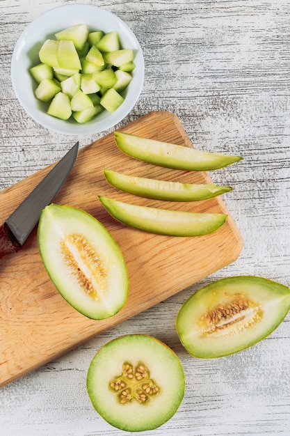 Melone a fette in un tagliere di legno con melone in ciotola e coltello piatto giaceva su uno sfondo di pietra bianca
