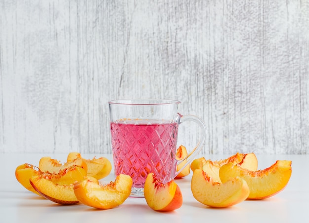 Free photo sliced nectarine with summer drink on white and grungy wall, side view.