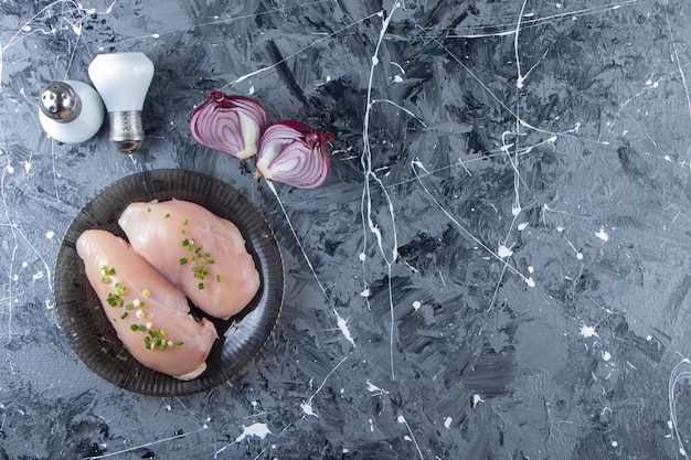 Sliced onion and chicken breast on a plate , on the marble background. 