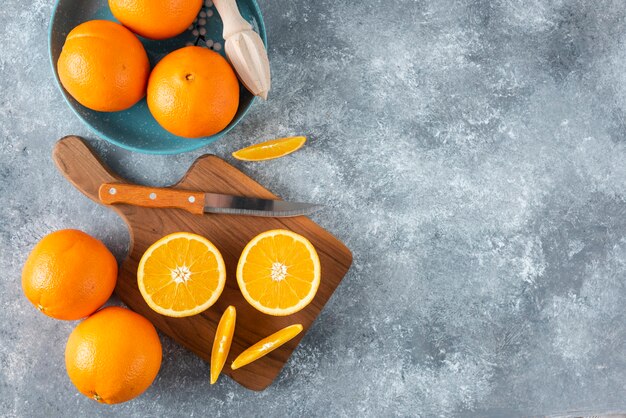Sliced orange fruits with whole oranges on a wooden board .