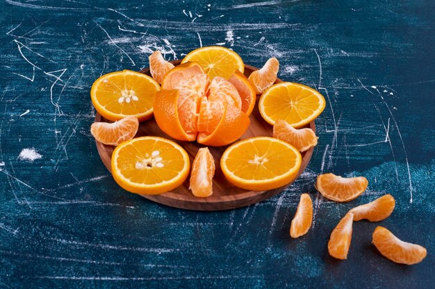 Sliced oranges and mandarines isolated on a wooden platter on blue background. High quality photo